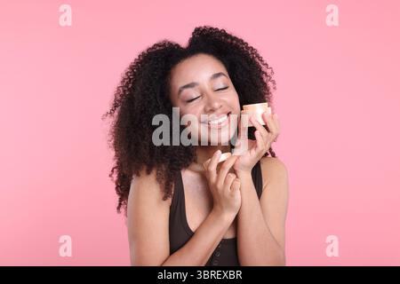 Schöne brasilianische Frau mit einem Glas Kollagencreme auf rosa Hintergrund Stockfoto