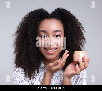 Schöne brasilianische Frau mit einem Glas Kollagencreme auf grauem Hintergrund Stockfoto