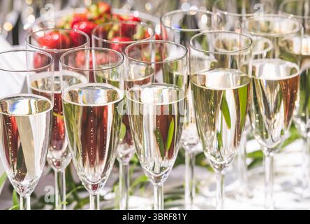 Sekt- oder Weißweinflöten mit Bläschen auf dem Tisch während einer Party im Freien unter der Sonne mit Erdbeeren im Hintergrund Stockfoto