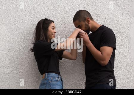 Ein Paar mit flachem Design lehnt sich an die Stuckwand, der Mann küsst die Hand der Frau mit einer Sonnenbrille Stockfoto