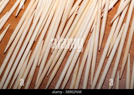 Lange Zahnstocher aus Holz sind kunstvoll auf einer warmen Holzoberfläche angeordnet. Stockfoto