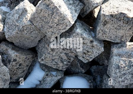 Große, raue Steine sind hoch gestapelt, teilweise mit Schneeflocken bedeckt. Stockfoto
