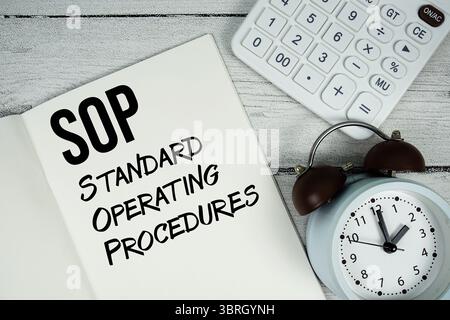 SOP Standard Operating Procedures Text auf Papier Notizbuchseite mit Wecker und Rechner auf hölzernem Hintergrund Stockfoto