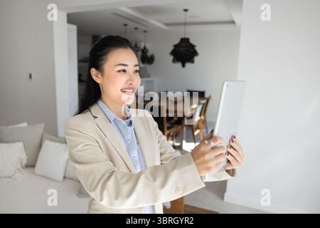 Frau, die ein Tablet hält, steht in einem stilvollen, modernen Wohnzimmer Stockfoto
