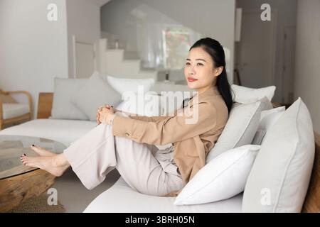 Nachdenkliche vietnamesische Frau in lässigen Kleidern, die sich zu Hause entspannt Stockfoto