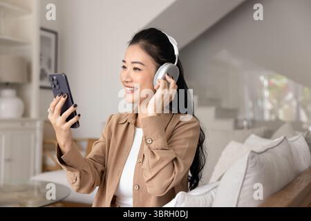 Frau trägt kabellose Kopfhörer und sieht Videoinhalte auf dem Mobiltelefon an Stockfoto