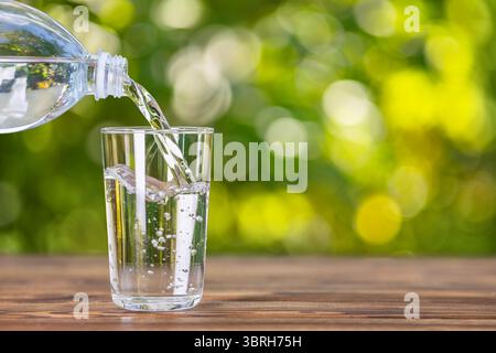 Trinken Sie Wasser aus der Plastikflasche, die auf einem Holztisch in Glas fließt Stockfoto