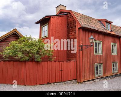 Sodertalje, Schweden - 6. Juni 2025: Ein bezauberndes rotes Holzhaus mit schrägem Dach und grünen Fensterrahmen, umgeben von einem Kiesweg und einem kleinen Bus Stockfoto