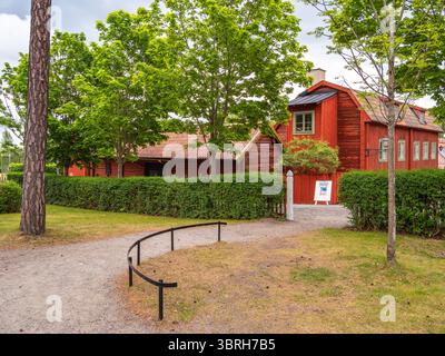 Sodertalje, Schweden - 6. Juni 2025: Ein bezauberndes rotes Holzhaus, umgeben von üppig grünen Bäumen und Sträuchern, mit einem gewundenen Kiesweg, der zum en führt Stockfoto