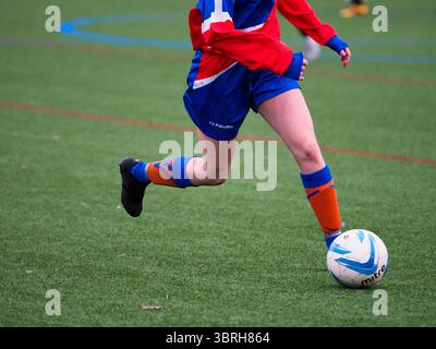 Eine Nahaufnahme einer Fußballspielerin, die während eines Fußballspiels auf einem Allwetterfeld mit dem Ball dribbelt Stockfoto