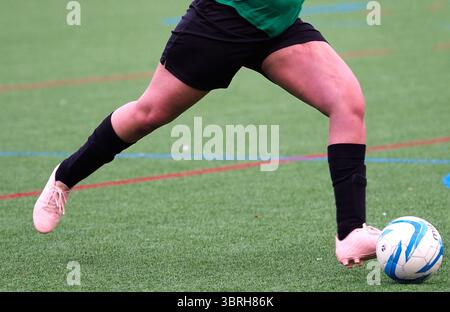 Eine Nahaufnahme einer Fußballspielerin, die während eines Fußballspiels auf einem Allwetterfeld mit dem Ball dribbelt Stockfoto