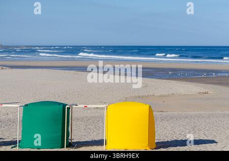 Farbenfrohe grüne und gelbe Strandhütten an einem breiten Sandstrand mit Meereswellen Stockfoto