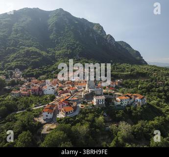 Blick aus der Vogelperspektive auf die Dächer von Terrakotta, die sich um den alten Turm gruppieren, vor dem Hintergrund der majestätischen grünen Berge, Summonte, Avellino, Italien. Stockfoto