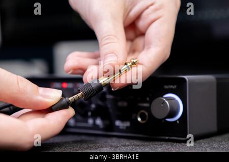 Detaillierte Nahaufnahme zeigt Hände, die einen goldenen Audiobuchsenadapter anschließen, ein wichtiger Schritt für die Einrichtung professioneller Audiosysteme für die Produktion Stockfoto