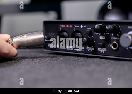 Nahaufnahme einer menschlichen Hand, die einen silbernen XLR-Audioanschluss in die Eingangsbuchse einer digitalen Soundkarte einsteckt, um die Einrichtung für die Studioarbeit anzuzeigen Stockfoto