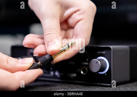 Detailaufnahme einer Hand, die eine goldene Audiobuchse an den AUSGANG eines dunklen Audiogeräts anschließt, zeigt die Einrichtung für Musikaufnahmen und professionelle aud Stockfoto