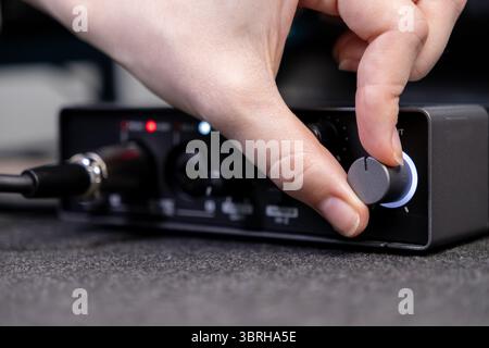 Nahaufnahme einer Hand, die ein Zifferblatt auf einer eleganten schwarzen Soundkarte dreht, um eine präzise Audiosteuerung für Aufnahme, Podcasting und digitale Inhalte anzuzeigen Stockfoto