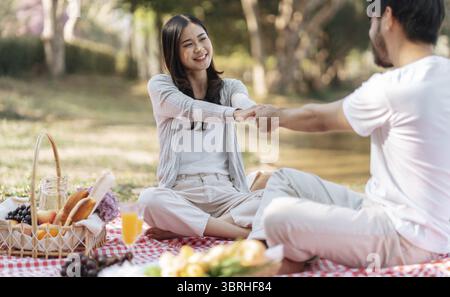 Glückliches romantisches Paar am Valentinstag asiatisches Paar hält Hände für einen kurzen Moment zusammen. Glückliches Paar, das sich mit Picknickkorb entspannt Stockfoto