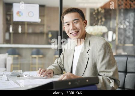 Lächelnder junger asiatischer Geschäftsmann im modernen Büro. Gutaussehender asiatischer Mann glücklich und freundlich während der Arbeit Erfolg Job Stockfoto