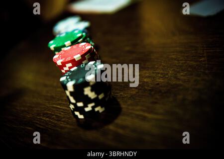 Eine Nahaufnahme aus einem niedrigen Winkel von gestapelten, bunten Poker-Chips (schwarz, rot, grün) auf einem dunklen Holztisch mit selektivem Fokus. Stockfoto