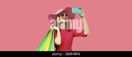 Porträt des schönen, glücklichen, lächelnden jungen Frauen-Models, das Selfie mit Handy macht, das bunte Einkaufstaschen in Sommer-Strohhut hält, Kleid auf der Nadel Stockfoto