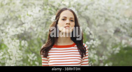 Porträt einer hübschen jungen Frau im Frühling blühenden Garten mit weißen Blumen auf den Bäumen im Park Stockfoto