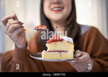 Schöne asiatische Frau, die leckeren Kuchen isst. Das Teenager-Mädchen isst den Kuchen Stockfoto