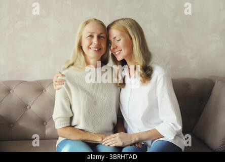Porträt einer glücklich lächelnden kaukasischen Mutter mittleren Alters, die ihre erwachsene Tochter zusammen umarmt und zu Hause auf der Couch sitzt Stockfoto