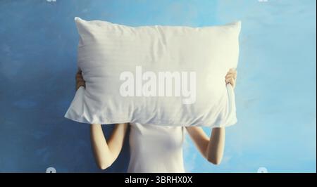 Gesunder Schlaf, müde Frau, die an Schlaflosigkeit leidet und zu Hause ihren Kopf mit weißem weichen Kissen bedeckt Stockfoto