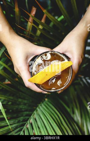 Orange Americano Iced Coffee in der Hand halten. Eisschwarzer Kaffee gemischt mit Orangensaft auf dem Tisch Stockfoto