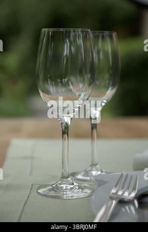 Zwei klare Weingläser stehen elegant auf einem ordentlich angeordneten Tisch. Die weiche grüne Tischdecke ergänzt die ruhige Umgebung im Freien, was darauf hindeutet Stockfoto