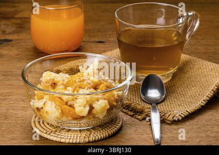 Köstlicher hausgemachter Pfirsichkuchen in transparenter Glasschüssel auf Bambusmatte mit einer Tasse heißem Tee auf Leintuch und frischem Orangensaft in einem Glas auf AA Stockfoto