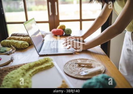 Kleine Unternehmen. Lächelnde junge Unternehmerin, asiatische Frau. Stanznadel-Handwerkerin mit Laptop-Computer in der Studio-Werkstatt. Handgefertigtes Handwerk Stockfoto