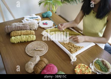Stanznadel. Asiatische Frau, die handgemachtes Hobby-Stricken in der Atelierwerkstatt herstellt. Designer-Arbeitsplatz Handgefertigtes Bastelprojekt DIY Stickkonzept Stockfoto