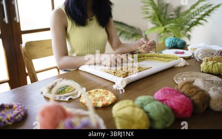 Stanznadel. Asiatische Frau, die handgemachtes Hobby-Stricken in der Atelierwerkstatt herstellt. Designer-Arbeitsplatz Handgefertigtes Bastelprojekt DIY Stickkonzept Stockfoto