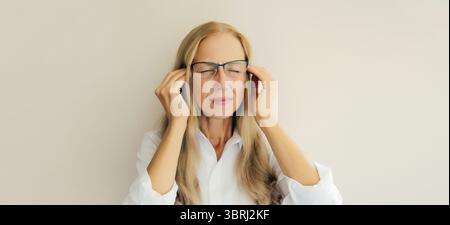 Erschöpfte, müde, kaukasische, reife Angestellte mit Kopfschmerzen, Stress, Müdigkeit, Schläfenschmerzen, leidet an Migräne, Spannung im Kopf im Büro Stockfoto