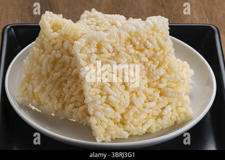 Nahansicht Stapel von quadratischen knusprigen Reiscrackern in weißer Keramikschale in schwarzer Keramikschale auf Holztisch Stockfoto