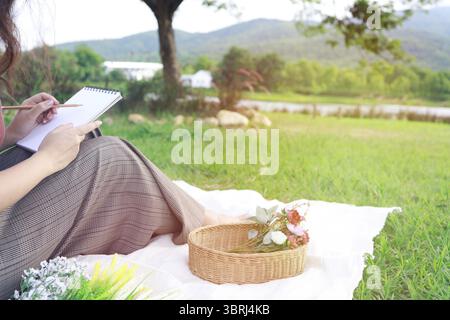 Allein asiatische Frau, die bei einem Picknick im Naturpark draußen am sonnigen Tag den Sommer genießt und träumt Stockfoto