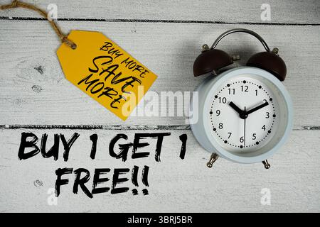 1 Kaufen Und 1 Gratis Erhalten!! Mehr kaufen Sparen Sie mehr mit Preisschild und Wecker auf hölzernem Hintergrund Stockfoto