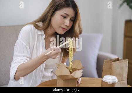 Asiatische Frau mit Essen und Getränken zum Mitnehmen zu Hause. Konsum Essen zu Hause Lieferessen. Genießen Sie köstliche Lieferung zum Mitnehmen leckere Mahlzeit Stockfoto