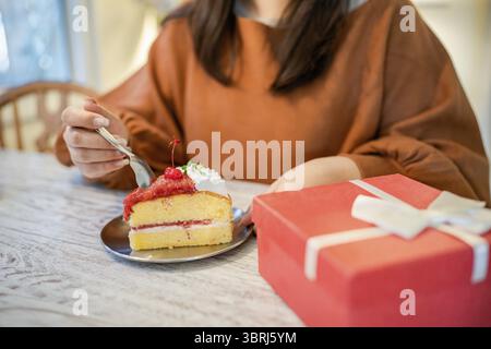 Glückliche asiatische Frau, die leckeren Weihnachts-Obstkuchen isst. Weihnachts-Dinner-Party mit leckerem Stück Weihnachtskuchen Neujahr und Weihnachtskonzepte Stockfoto