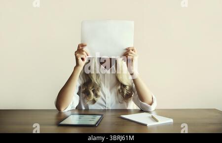 Frau zeigt und hält ein weißes leeres Blatt Papier für Textkopierraum, während sie mit einem digitalen Tablet-Computer am Schreibtisch arbeitet Stockfoto