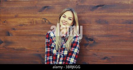 Porträt der schönen kaukasischen blonden, lächelnden jungen Frau in lässigem kariertem Hemd in der Stadt Stockfoto