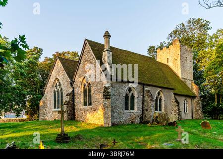 Die Steinkirche St. Augustinus aus dem 13. Jahrhundert im Dorf Snave in Kent mit Gräbern auf dem Friedhof in der frühen goldenen Stunde. Stockfoto