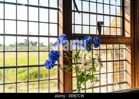 Ausstellung von blauen und weißen Plastikblumen in einem alten Kirchenfenster der Fairfield Kirche St. Thomas A Becket auf Romney Marsh. Stockfoto
