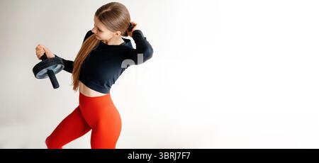 Blick aus der Höhe auf eine attraktive schlanke Dame in stilvoller Trainingskleidung, die mit Kurzhanteln und verstellbarem Haar steht. Blonde, kaukasische Dame, die physisch arbeitet Stockfoto