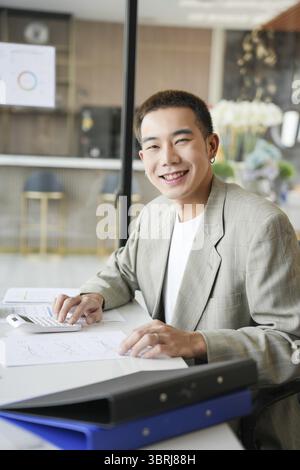 Lächelnder junger asiatischer Geschäftsmann im modernen Büro. Gutaussehender asiatischer Mann glücklich und freundlich während der Arbeit Erfolg Job Stockfoto