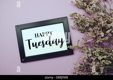 Happy Tuesday Text mit Blumenstrauß Dekoration auf lila Hintergrund Stockfoto