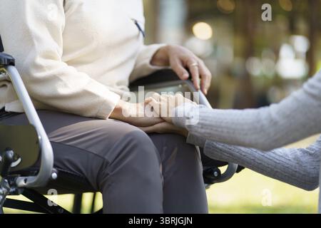 Familienbeziehung Asiatische Seniorin im Rollstuhl mit glücklicher Tochter, die während des gemeinsamen Aufenthalts eine Pflegekraft hält Stockfoto
