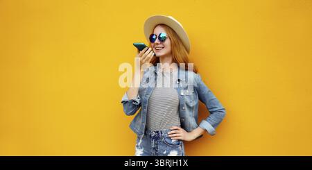 Glückliche junge Frau, die am Telefon telefoniert, mit Sprachaufzeichnungsgerät, Assistent oder nimmt Anrufe in lässiger Kleidung auf farbenfroher gelber Ba entgegen Stockfoto